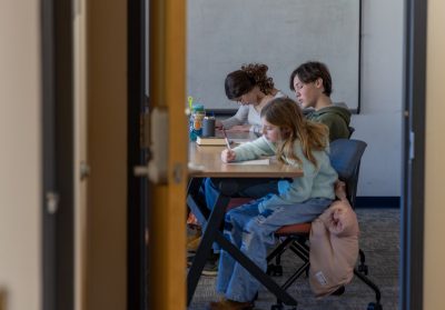 A group of three students are sitting at a desk and filling out a worksheet.